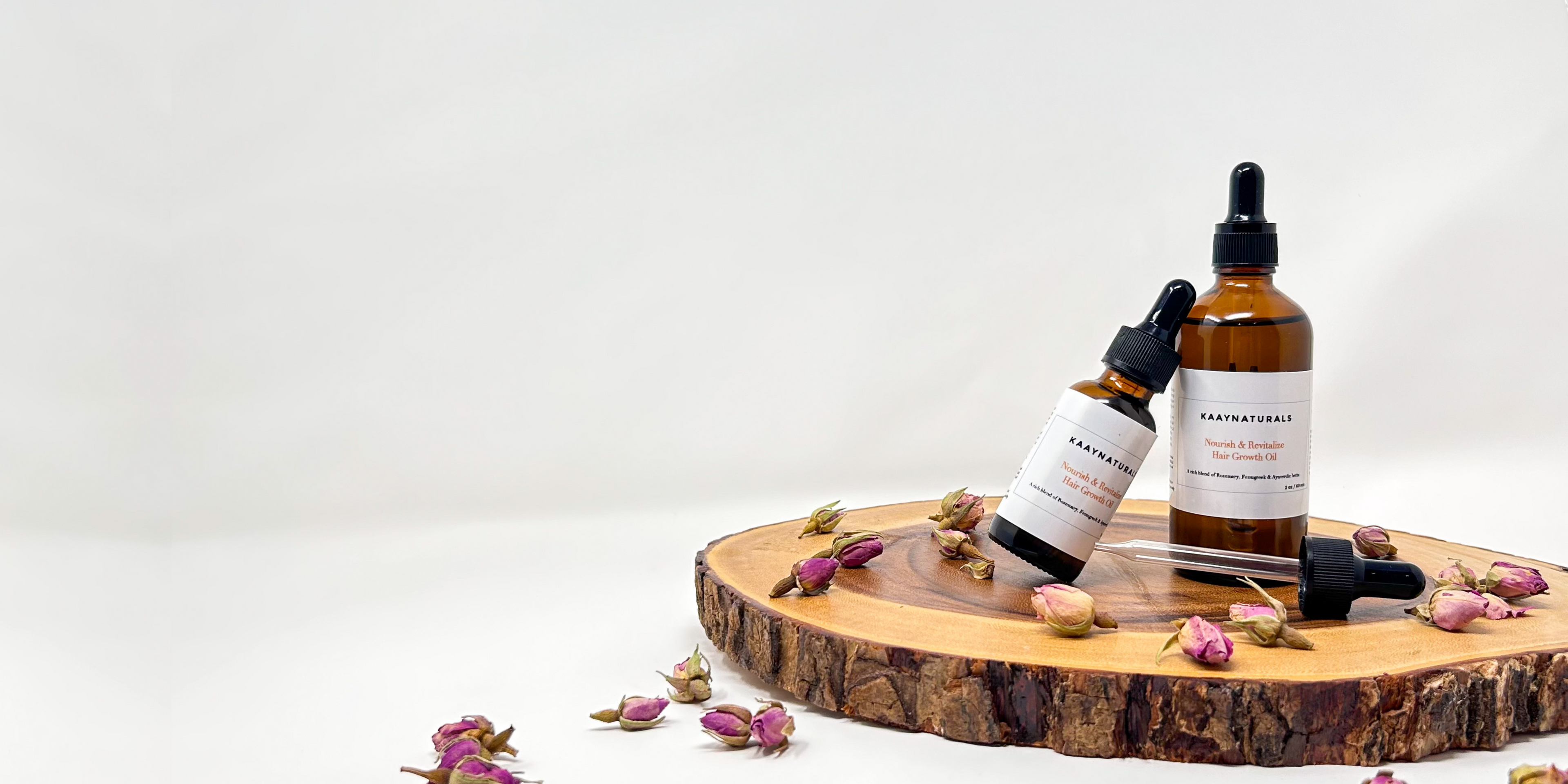 Bottle of Earthly Organics hair oil on a wooden board with flowers on a white background