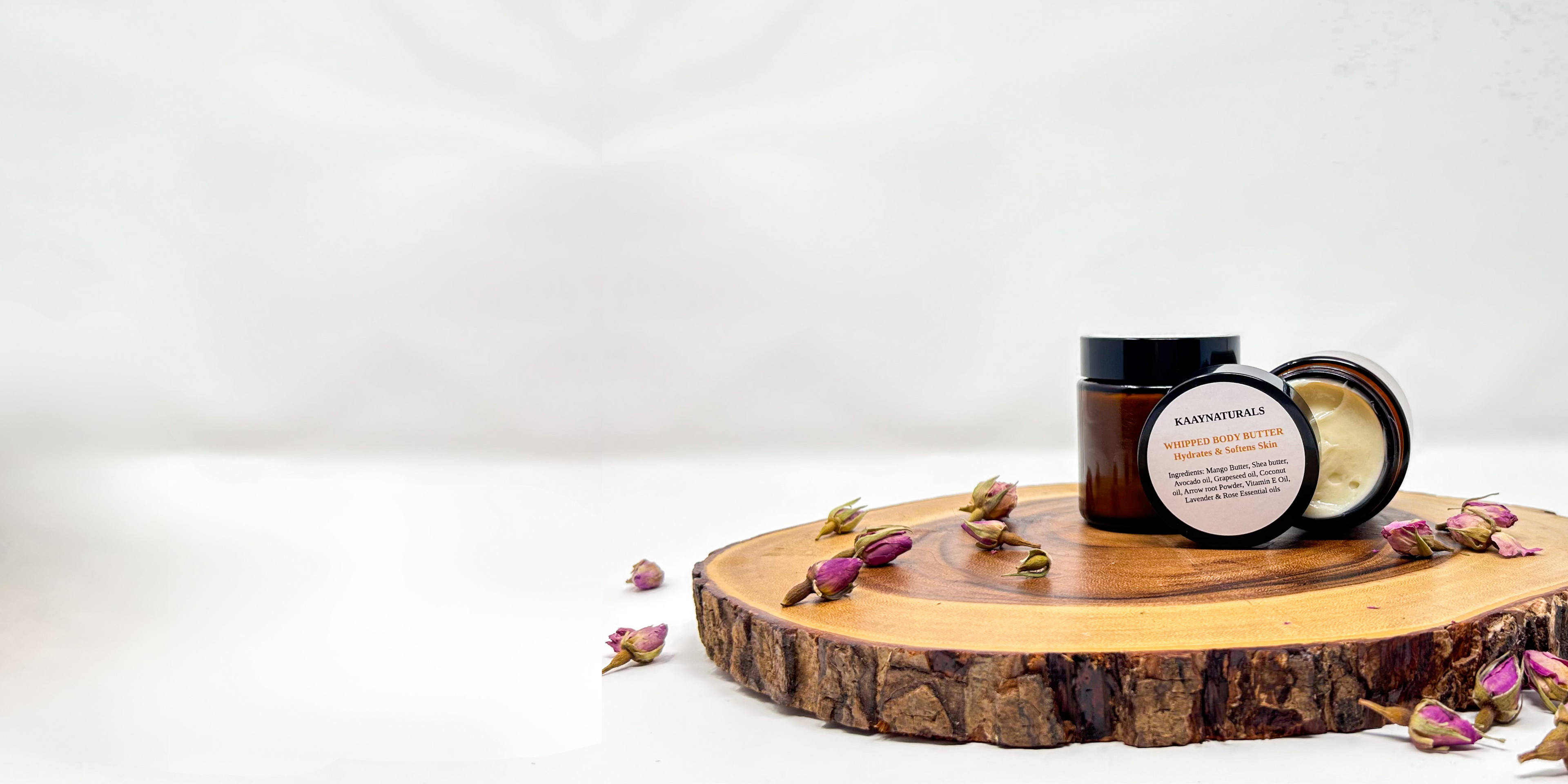 whipped luxurious body butter on a wooden tray surrounded by rose petals