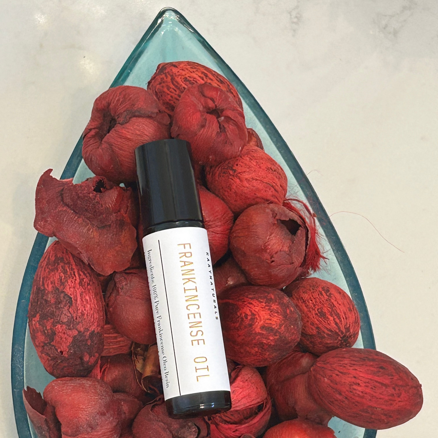 Roller bottle of frankincense oil on a bed of red树脂 balls in a glass dish.